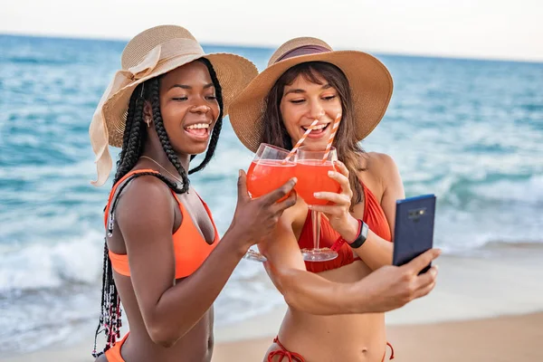 Mulheres batendo bebidas e tomando selfie na praia — Fotografia de Stock