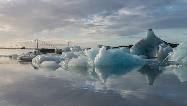 Reflektion av isbitar och hängbro på Glaciärlagunen Glacier Lagoon under sunrise — Stockfoto