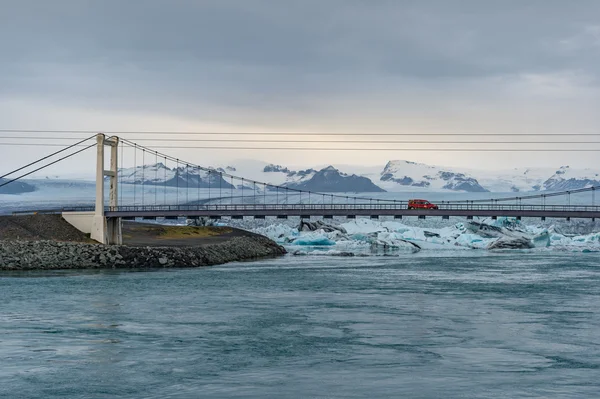 Ponte sospeso sullo stretto mare con la laguna del ghiacciaio Jokulsarlon e lo sfondo della montagna innevata — Foto Stock