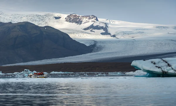 Туристическая лодка на ледниковой лагуне Джоколсарлон на фоне снежных гор — стоковое фото