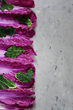 Mor Çin lahanasından taze yapraklar ve gri arka planda yeşil lahana yaprakları. Düz yatıyordu. Mevsimlik sebzeler, üst manzara.