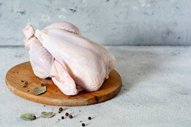 Çiğ tavuk leşi, gri bir arka planda kesim tahtasının üzerinde pişmeye hazır..