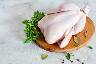 Çiğ tavuk leşi, gri bir arka planda kesim tahtasının üzerinde pişmeye hazır..