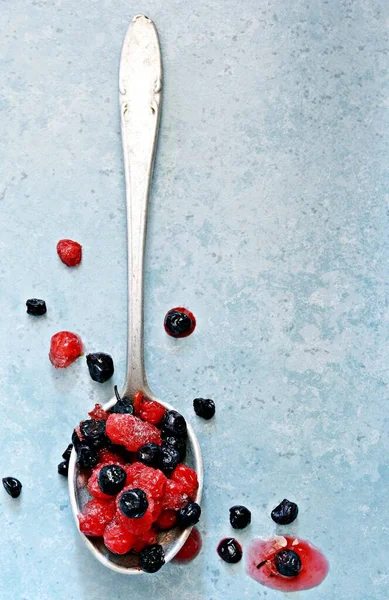 Frozen (thawed) cherries, blueberries, red currants in a spoon on a blue background. Healthy fruits, homemade preparations for making smoothies, compote, fruit drink, fruit puree.