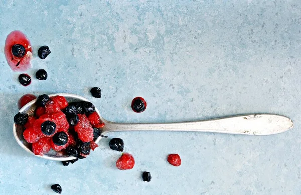 Frozen (thawed) cherries, blueberries, red currants in a spoon on a blue background. Healthy fruits, homemade preparations for making smoothies, compote, fruit drink, fruit puree.