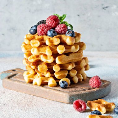 Kahvaltıda olgun böğürtlenli (ahududu, yaban mersini, böğürtlen) taze Belçika waffle 'ları, açık arkaplanda tahta üzerinde nane ve pudra şekeri.