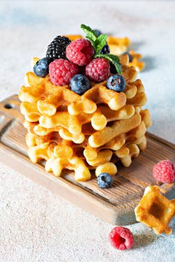Kahvaltıda olgun böğürtlenli (ahududu, yaban mersini, böğürtlen) taze Belçika waffle 'ları, açık arkaplanda tahta üzerinde nane ve pudra şekeri.