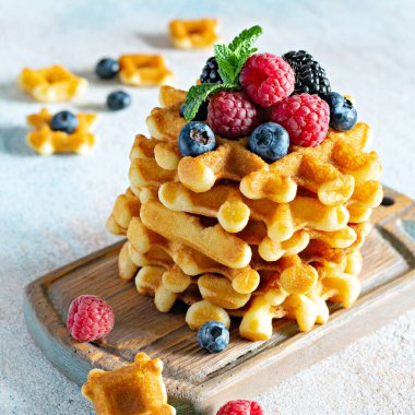 Kahvaltıda olgun böğürtlenli (ahududu, yaban mersini, böğürtlen) taze Belçika waffle 'ları, açık arkaplanda tahta üzerinde nane ve pudra şekeri.