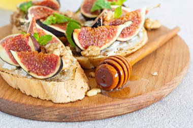 Yumuşak ricotta, olgun incir, ceviz ve çam fıstığı, nane ve bal arkaplanda çıtır bruschetta. Tahtada ballı ve cevizli incirli tost..