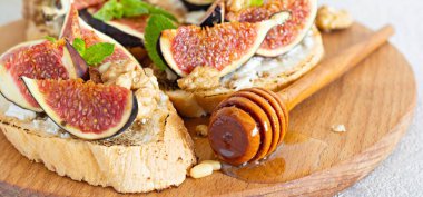 Yumuşak ricotta, olgun incir, ceviz ve çam fıstığı, nane ve bal arkaplanda çıtır bruschetta. Tahtada ballı ve cevizli incirli tost..