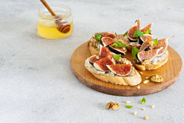 Hafif arkaplanda yumuşak ricotta, olgun incir, ceviz ve çam fıstığı, nane ve bal ile gevrek bruschetta (tost). Tahtada ballı ve cevizli incirli tost..