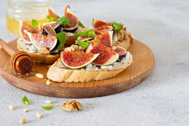 Hafif arkaplanda yumuşak ricotta, olgun incir, ceviz ve çam fıstığı, nane ve bal ile gevrek bruschetta (tost). Tahtada ballı ve cevizli incirli tost..