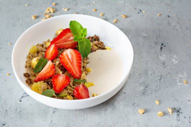 Beyaz bir tabakta fındıklı, kurutulmuş meyveli gevrek, taze çilek, nane ve yoğurt (mayalanmış süt). Sağlıklı kahvaltı kavramı.