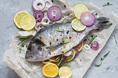 Taze balık dorado. Çiğ dorado, bitkiler, baharatlar, limon ve limon dilimleri gri arka planda pişirmeye hazır. Üst Manzara. Taze balık yaldızlı, tuzlu, otlu ve biberli..