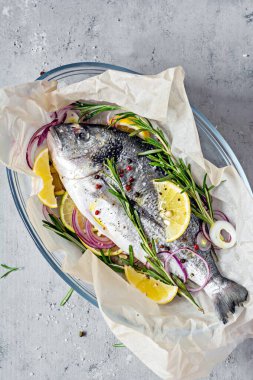 Taze balık dorado. Çiğ dorado, bitkiler, baharatlar, limon ve limon dilimleri gri arka planda pişirmeye hazır. Üst Manzara. Taze balık yaldızlı, tuzlu, otlu ve biberli..