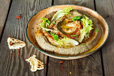 An oriental dish of baked eggplant babaganush (eggplant puree) with spices, herbs, lettuce and oriental flatbreads on wooden background. clipart