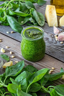 Taze fesleğen yaprağı, çam fıstığı, parmesan, sarımsak ve ahşap zemin üzerinde zeytinyağından yapılmış cam bir kavanozda yeşil pesto. Salata, makarna ve pizza için popüler İtalyan sosu..
