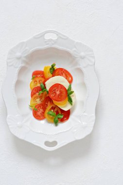 Caprese. Beyaz arka planda seramik bir kasede taze domates ve fesleğen yaprakları. Ev yapımı yemek. Lezzetli ve sağlıklı bir aperatif için konsept, düz yat. 