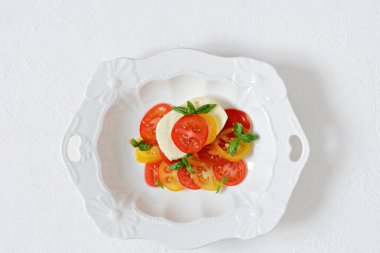 Caprese. Beyaz arka planda seramik bir kasede taze domates ve fesleğen yaprakları. Ev yapımı yemek. Lezzetli ve sağlıklı bir aperatif için konsept, düz yat. 