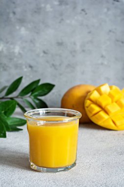 Bardakta taze mango suyu ve gri arka planda mango dilimi. Egzotik içecek, kopyalama alanı. Yılın moda renkleri