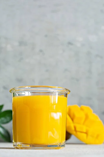 Fresh mango juice in a glass glass with mango slice on a gray background. Exotic drink, copy space. Trending colors of the year