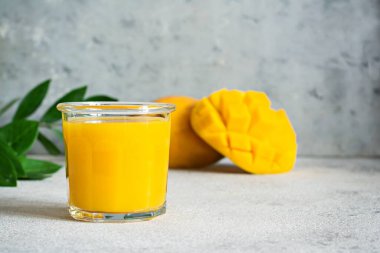 Bardakta taze mango suyu ve gri arka planda mango dilimi. Egzotik içecek, kopyalama alanı. Yılın moda renkleri