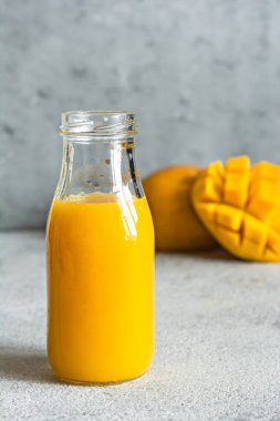 Bardakta taze mango suyu ve gri arka planda mango dilimi. Egzotik içecek, kopyalama alanı. Yılın moda renkleri