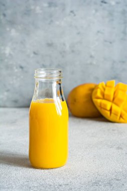 Bardakta taze mango suyu ve gri arka planda mango dilimi. Egzotik içecek, kopyalama alanı. Yılın moda renkleri