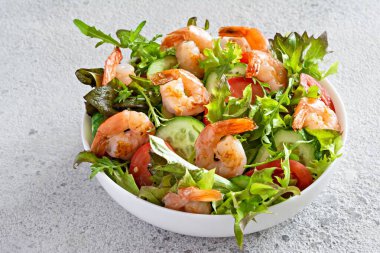 Hafif arkaplanda beyaz bir tabakta sebzeli taze çıtır salata ve deniz ürünleri (karides). Sağlıklı gıda konsepti.