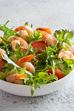 Hafif arkaplanda beyaz bir tabakta sebzeli taze çıtır salata ve deniz ürünleri (karides). Sağlıklı gıda konsepti.