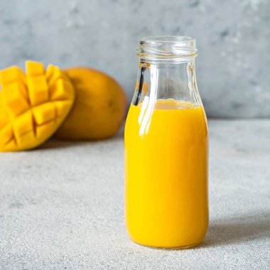 Bardakta taze mango suyu ve gri arka planda mango dilimi. Egzotik içecek, kopyalama alanı. Yılın moda renkleri