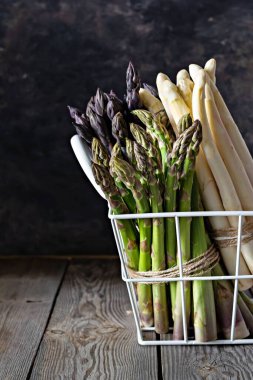 Koyu beyaz, mor, yeşil kuşkonmaz sepetin içinde, ahşap bir arka planda. Çiğ gıda konsepti, kopyalama alanı.