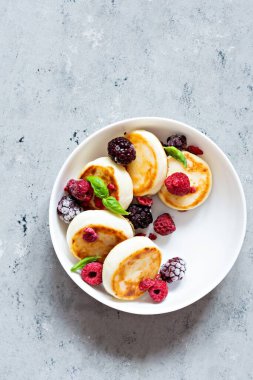 Taze süzme peynir ya da ricotta krepleri (şurup, börek) mavi arka planda taze böğürtlenli beyaz bir tabakta. Lezzetli sağlıklı kahvaltı. Ukrayna mutfağı, Rus mutfağı tatlı yiyecekler.