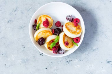 Taze süzme peynir ya da ricotta krepleri (şurup, börek) mavi arka planda taze böğürtlenli beyaz bir tabakta. Lezzetli sağlıklı kahvaltı. Ukrayna mutfağı, Rus mutfağı tatlı yiyecekler.