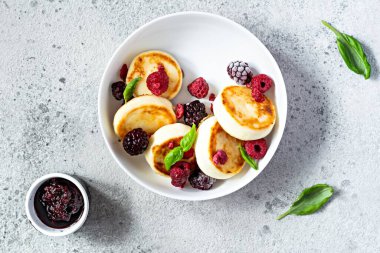 Taze süzme peynir ya da ricotta krepleri (şurup, börek) mavi arka planda taze böğürtlenli beyaz bir tabakta. Lezzetli sağlıklı kahvaltı. Ukrayna mutfağı, Rus mutfağı tatlı yiyecekler.