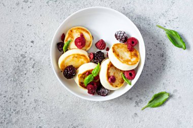 Taze süzme peynir ya da ricotta krepleri (şurup, börek) mavi arka planda taze böğürtlenli beyaz bir tabakta. Lezzetli sağlıklı kahvaltı. Ukrayna mutfağı, Rus mutfağı tatlı yiyecekler.