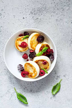 Taze süzme peynir ya da ricotta krepleri (şurup, börek) mavi arka planda taze böğürtlenli beyaz bir tabakta. Lezzetli sağlıklı kahvaltı. Ukrayna mutfağı, Rus mutfağı tatlı yiyecekler.