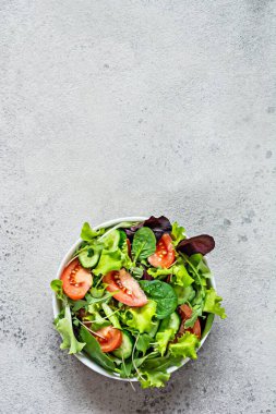 Taze sebzeli taze salata, olgun domatesler, salatalık, salatalık ve mikroyeşil gri arka planda bir kasede. Sağlıklı çiğ gıda konsepti. Metin için yer, kopyalama alanı.