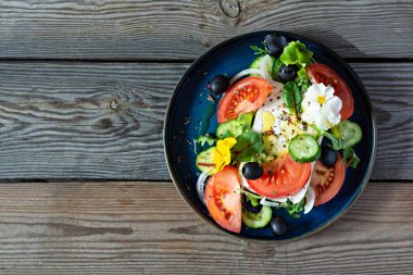Peynirli iştah açıcı salata, taze sebze (domates, salatalık, soğan), çıtır marul, mikroyeşillik ve menekşe çiçeği. Ahşap arka planda Yunan salatası. Çiçekli yemek.