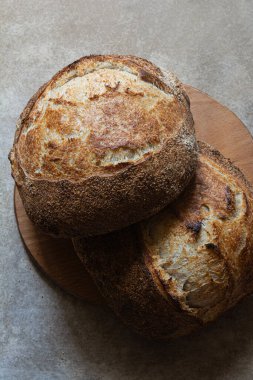 Gri bir arka planda tam buğday unu eklenmiş taze kabuklu ekşi ekmek. Mayasız ekmek, Tartine, sağlıklı yemek..