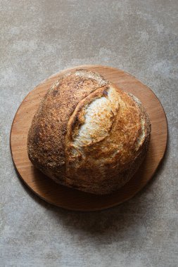 Gri bir arka planda tam buğday unu eklenmiş taze kabuklu ekşi ekmek. Mayasız ekmek, Tartine, sağlıklı yemek..