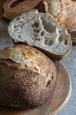 Gri bir arka planda tam buğday unu eklenmiş taze kabuklu ekşi ekmek. Mayasız ekmek, Tartine, sağlıklı yemek..
