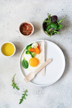 Healthy breakfast of fried egg and boiled vegetables with spinach on a light background. Healthy food concept, minimalism, top view.
