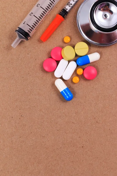 Stetoscopio rosso, siringhe e molte pillole colorate su sfondo di carta artigianale marrone . — Foto Stock