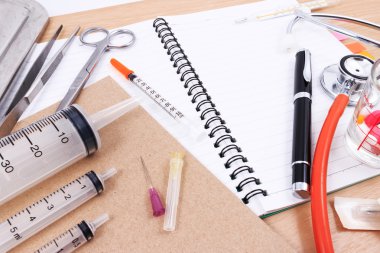 Stetoskop, şırınga, makas, kalem ve forseps beyaz tıbbi çalışma yüzeyi.