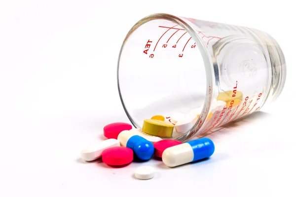 Molte pillole colorate in un misurino di vetro su sfondo bianco . — Foto Stock