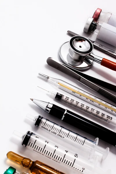 Estetoscopio, jeringas, tijeras, fórceps y ampollas sobre una superficie de trabajo médica blanca . — Foto de Stock