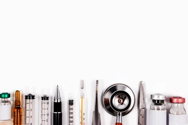 Stetoskop, sprutor, sax, pincett och ampuller på en vit medicinska arbetsyta. — Stockfoto