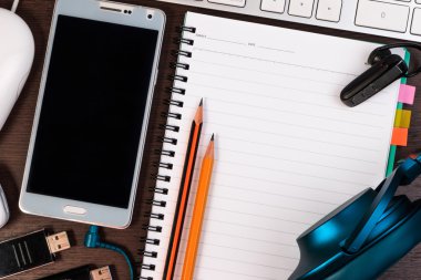 Cep telefonu, klavye, not defteri ve kalem bir tablo.