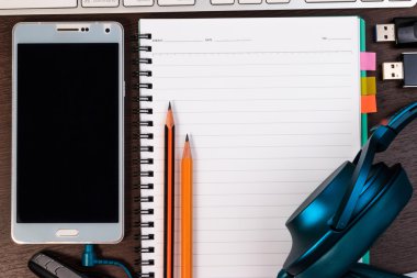 Cep telefonu, klavye, not defteri ve kalem bir tablo.
